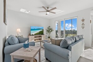 Ein modernes Wohnzimmer mit einer Couch, einem Couchtisch, einem Fernseher und einem Balkon mit Blick.