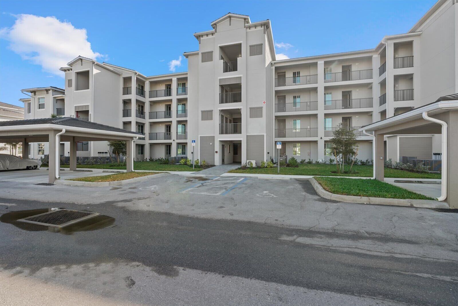 Un immeuble résidentiel à plusieurs étages, doté de balcons, d’un espace de stationnement couvert et d’une entrée aménagée.