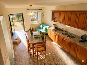 Une cuisine avec des meubles en bois, un coin repas avec une table et des chaises, et une vue sur un jardin grâce à une porte coulissante.