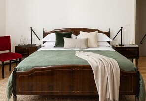 A neatly made bed with a wooden headboard, a green bedspread, and multiple pillows. There are two bedside tables with lamps and a red chair. - Cozy apartment for families and couples, proximity to Cansiglio Golf Club. (Osigo)