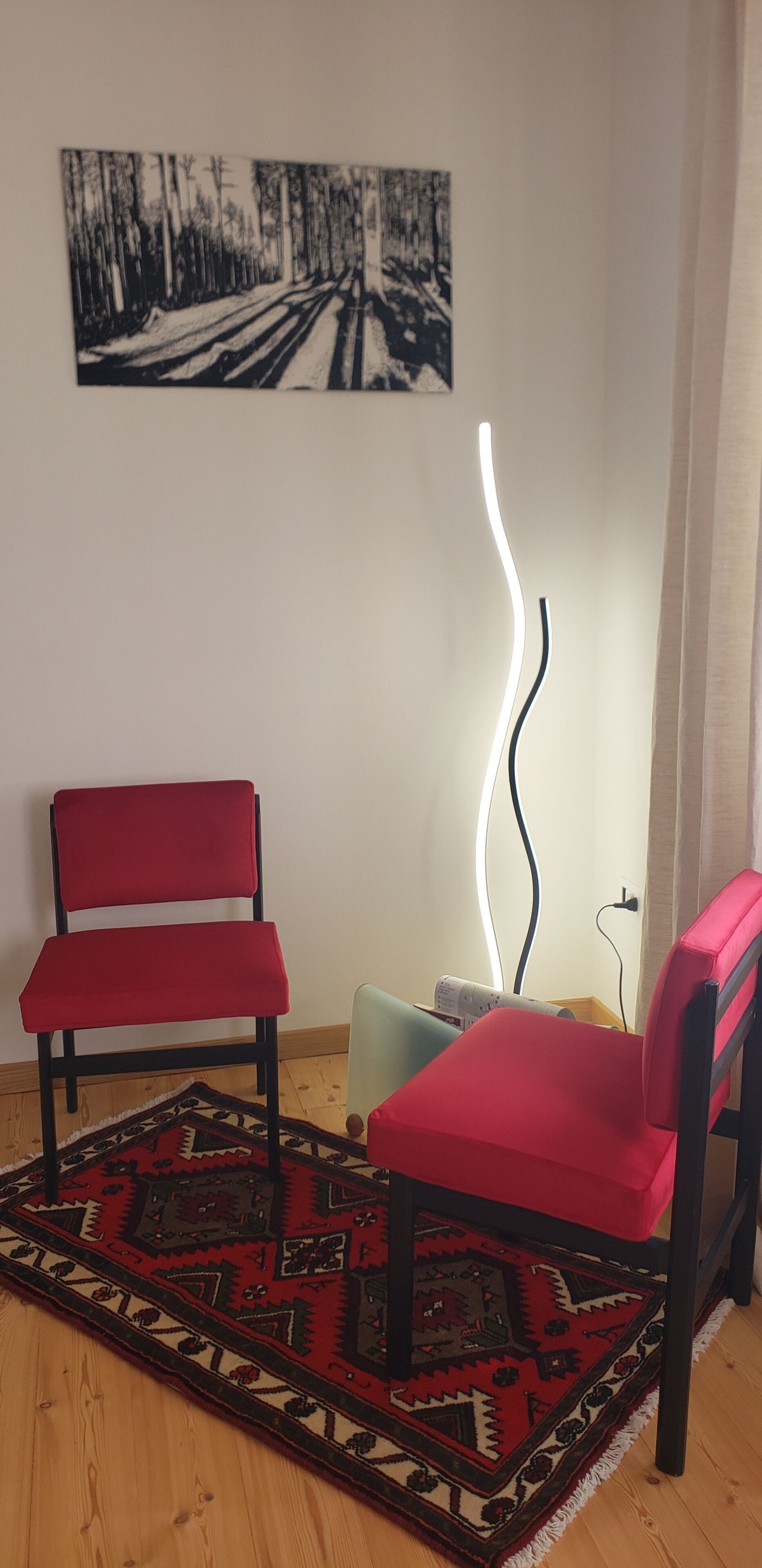 A room with two red chairs, a patterned rug, a wall-mounted light, and a painting.