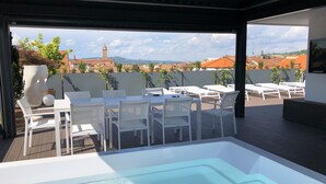 A rooftop terrace with a hot tub, white furniture, and a view of buildings and a tower. - Exclusive penthouse in the historic center of Alba, panoramic terrace with garden and private  pool and solarium. (alba)
