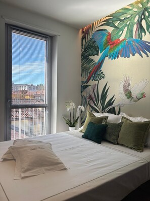 A bedroom with a bed, pillows, a window with blinds, a wall mural, and a potted orchid. - Exclusive penthouse in the historic center of Alba, panoramic terrace with garden and private  pool and solarium. (alba)