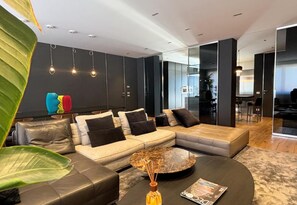 A modern living room with a sectional sofa, a coffee table, and a large plant. - Exclusive penthouse in the historic center of Alba, panoramic terrace with garden and private  pool and solarium. (alba)