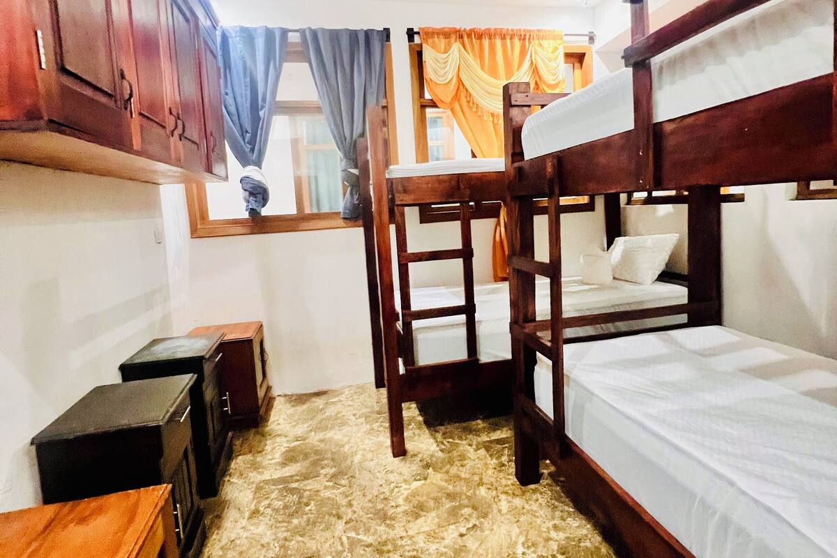 A bunk bed room with a wooden headboard, a small desk, and a window with curtains.