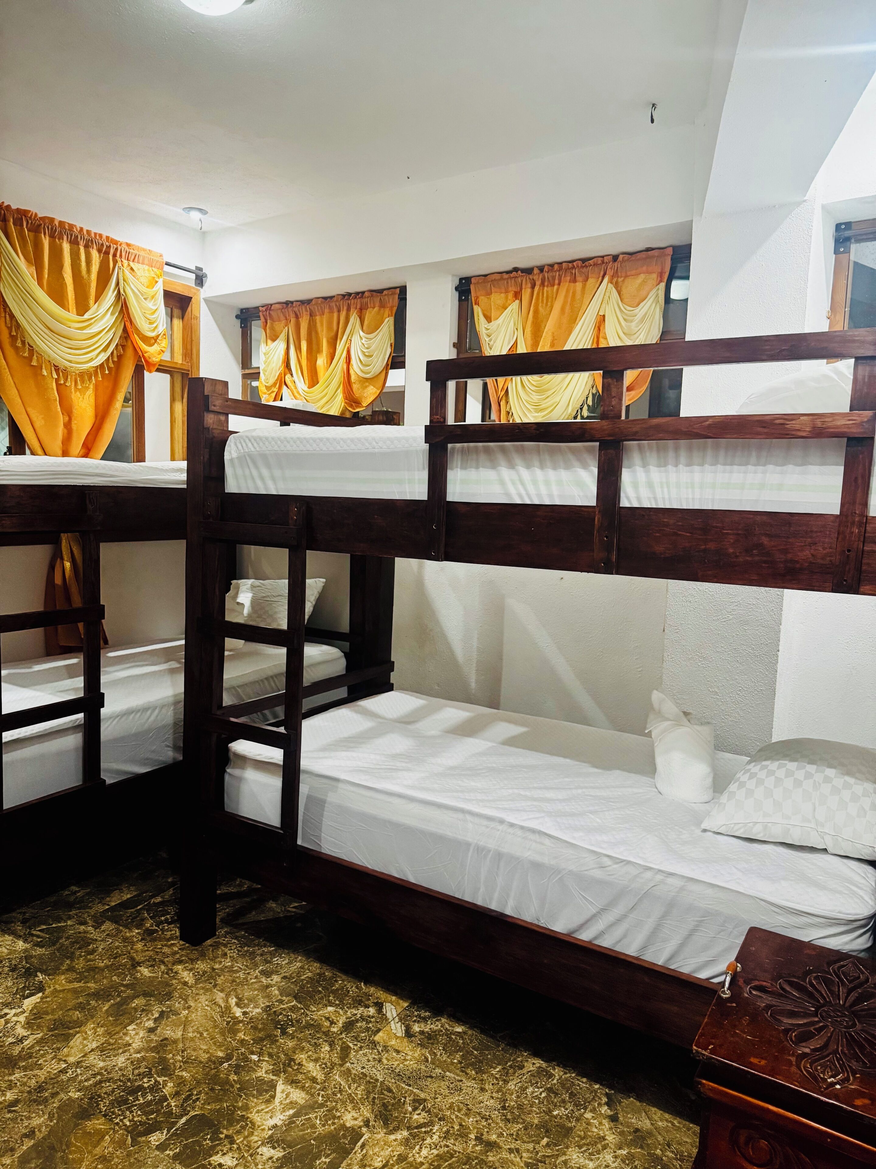 Dormitorio con literas de madera, ropa de cama blanca y cortinas amarillas.