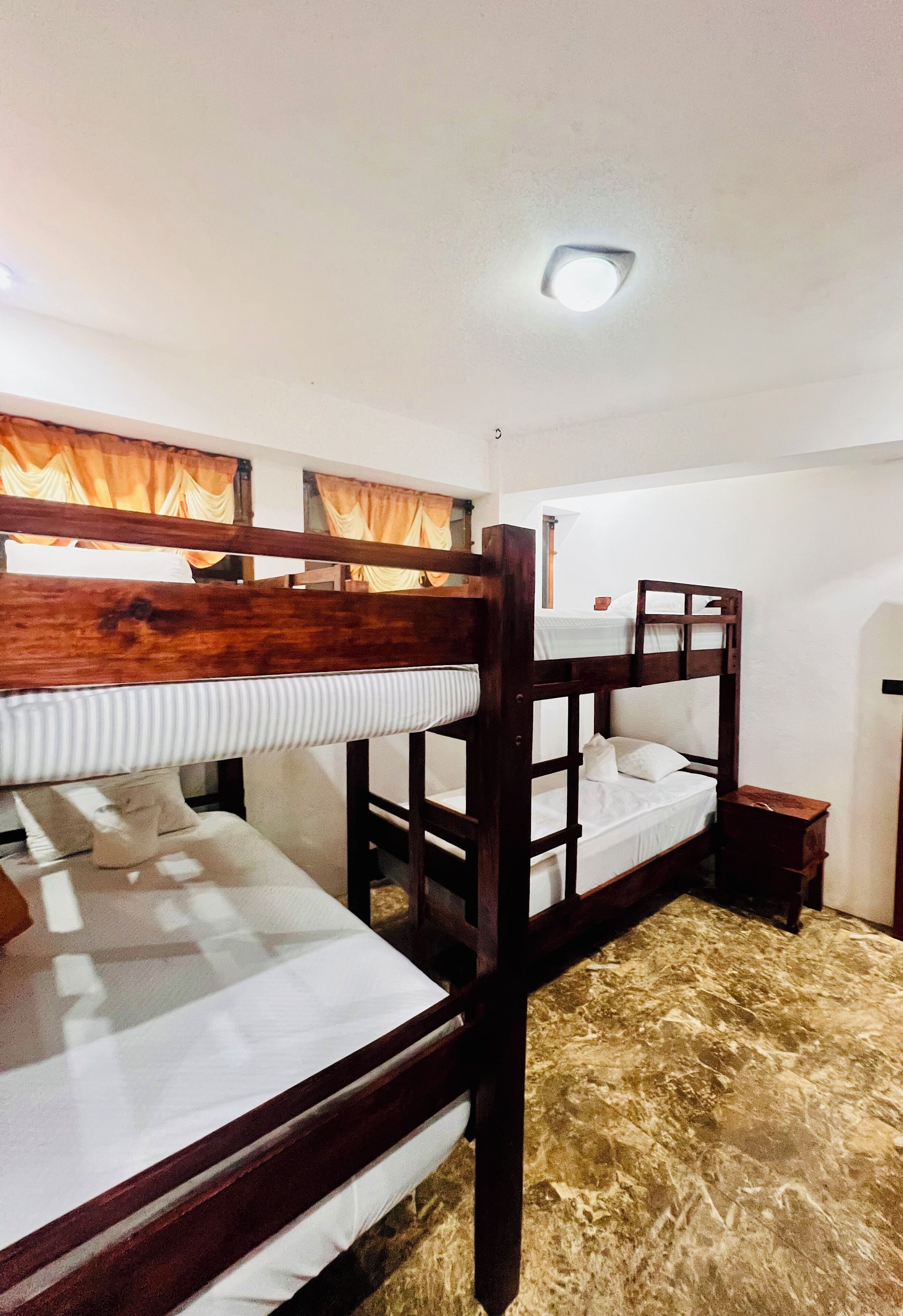 Dormitorio con literas, una lámpara en el techo, cabecero de madera y una mesita de noche pequeña.