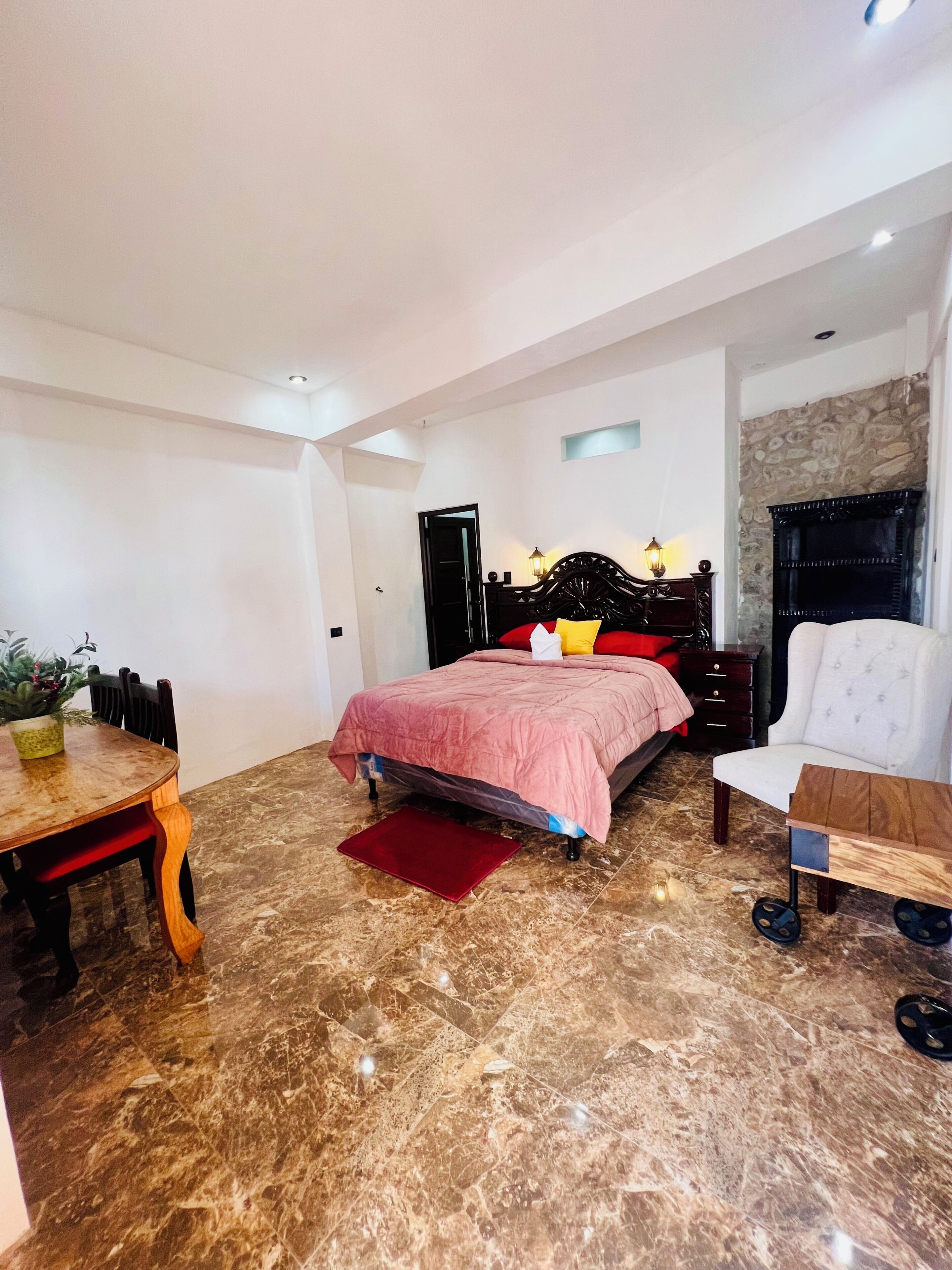 Un dormitorio con cama, una silla, una mesa y una planta en maceta.