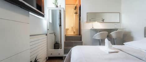 A modern hotel room with a bed, a desk, a chair, a mirror, and a staircase leading to a bathroom.
