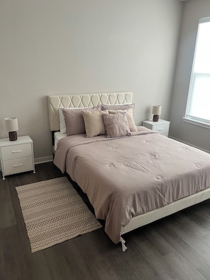 Un dormitorio con cama, dos mesitas de noche, una lámpara y un tapete estampado, además de una ventana.