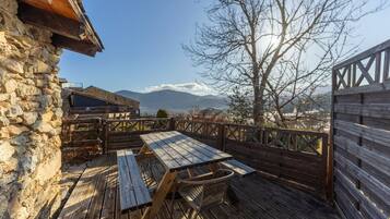 Terraza de madera con mesa y sillas, paredes de piedra y vista a las montañas.