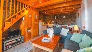 A cozy living room with a wooden staircase, a sofa, a coffee table, and a television. - La Grange de la Petite Ourse with Large Furnished Terrace, Stunning Lake and Mountain Views (Les Angles)