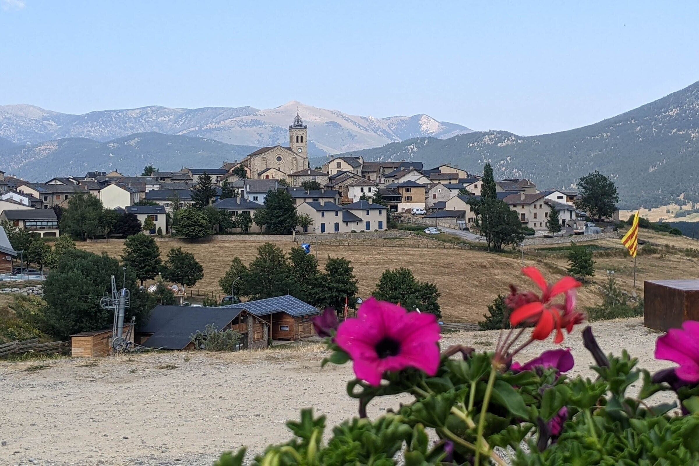 A village with traditional buildings, a church with a bell tower, and mountains in the background.