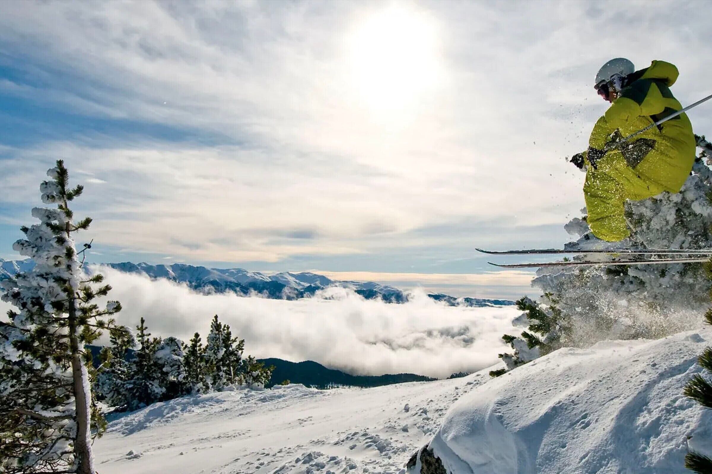 Eine verschneite Berglandschaft mit einem Skifahrer in gelber Ausrüstung.