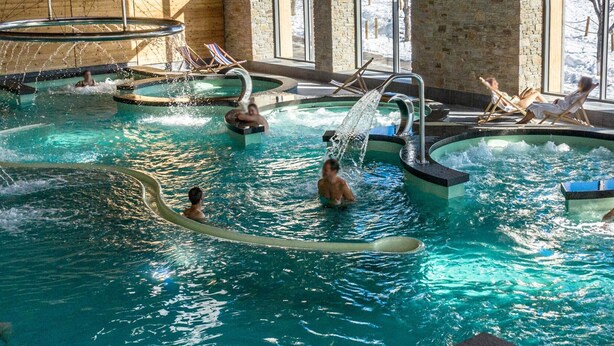 Piscina interna com vários elementos aquáticos e espreguiçadeiras.