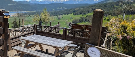 A wooden deck with picnic tables and chairs overlooking a mountainous landscape.