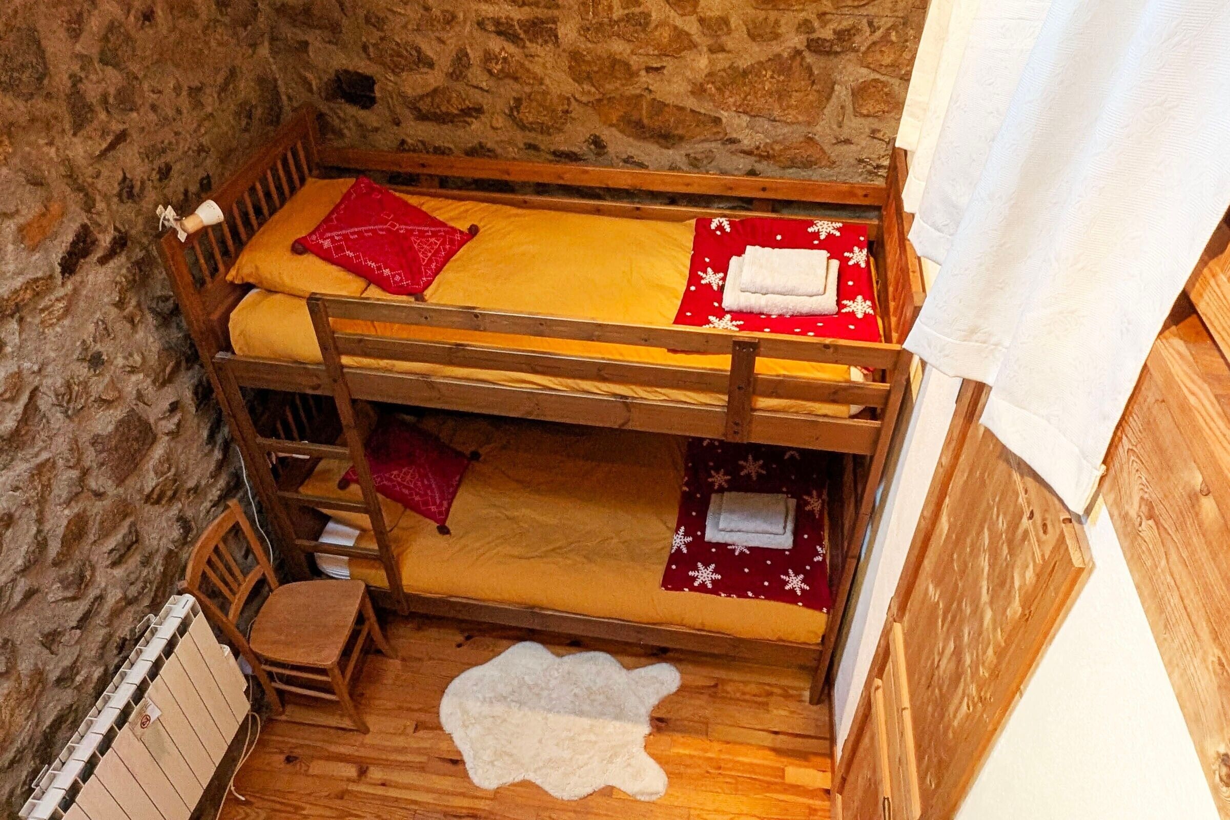 Une chambre avec des lits superposés, un mur en pierre, un plancher en bois et un tapis en fourrure blanche.