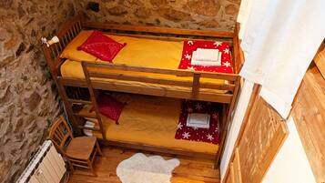 Une chambre avec des lits superposés, un mur en pierre, un plancher en bois et un tapis en fourrure blanche.