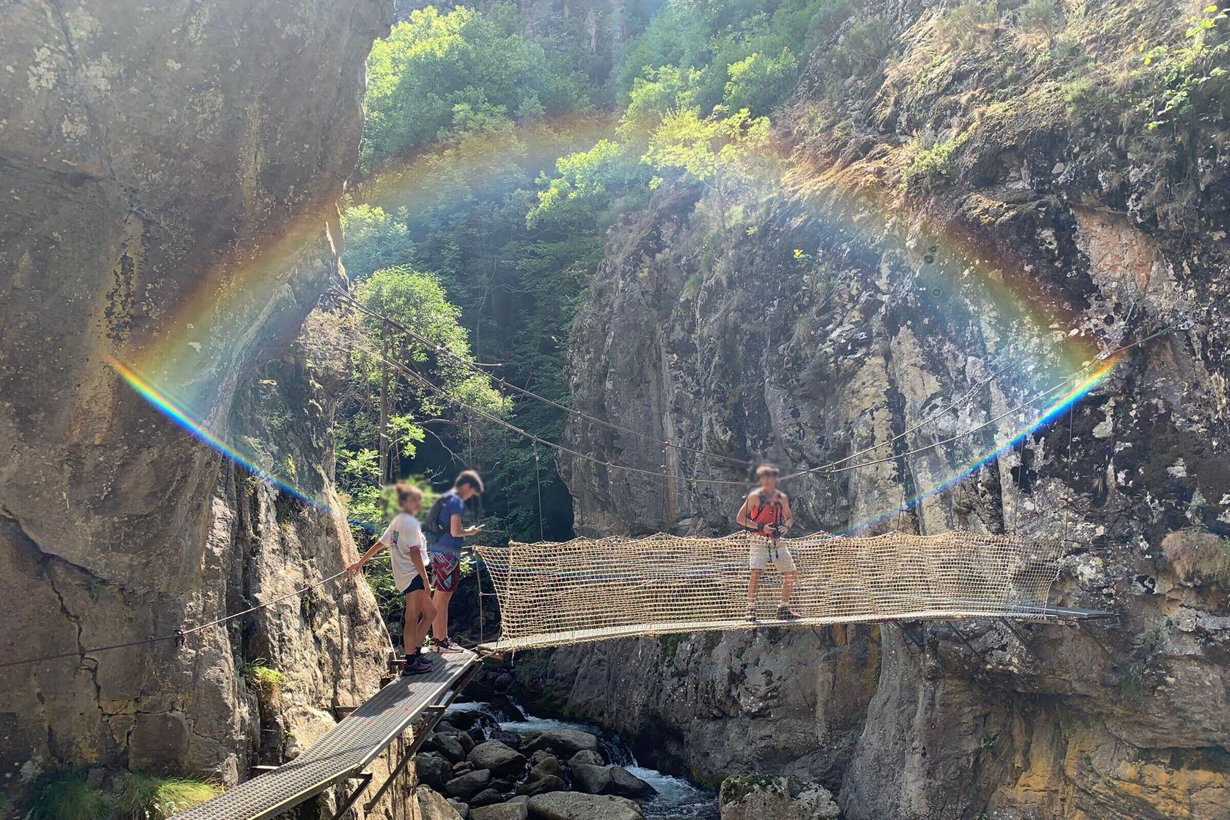 A suspension bridge over a rocky gorge with a rainbow visible in the background.