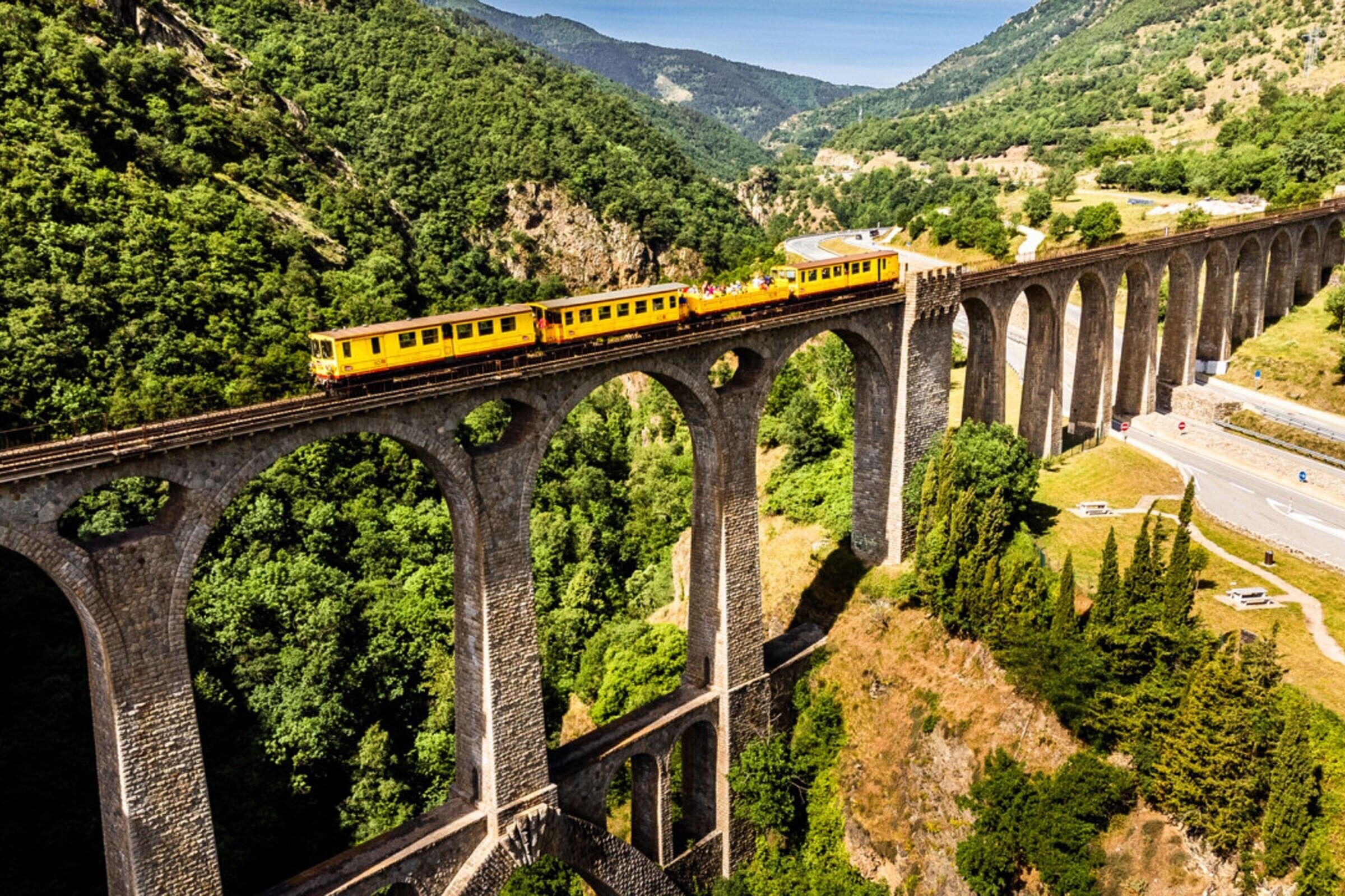 A train on a bridge with multiple arches, surrounded by lush greenery and hills.