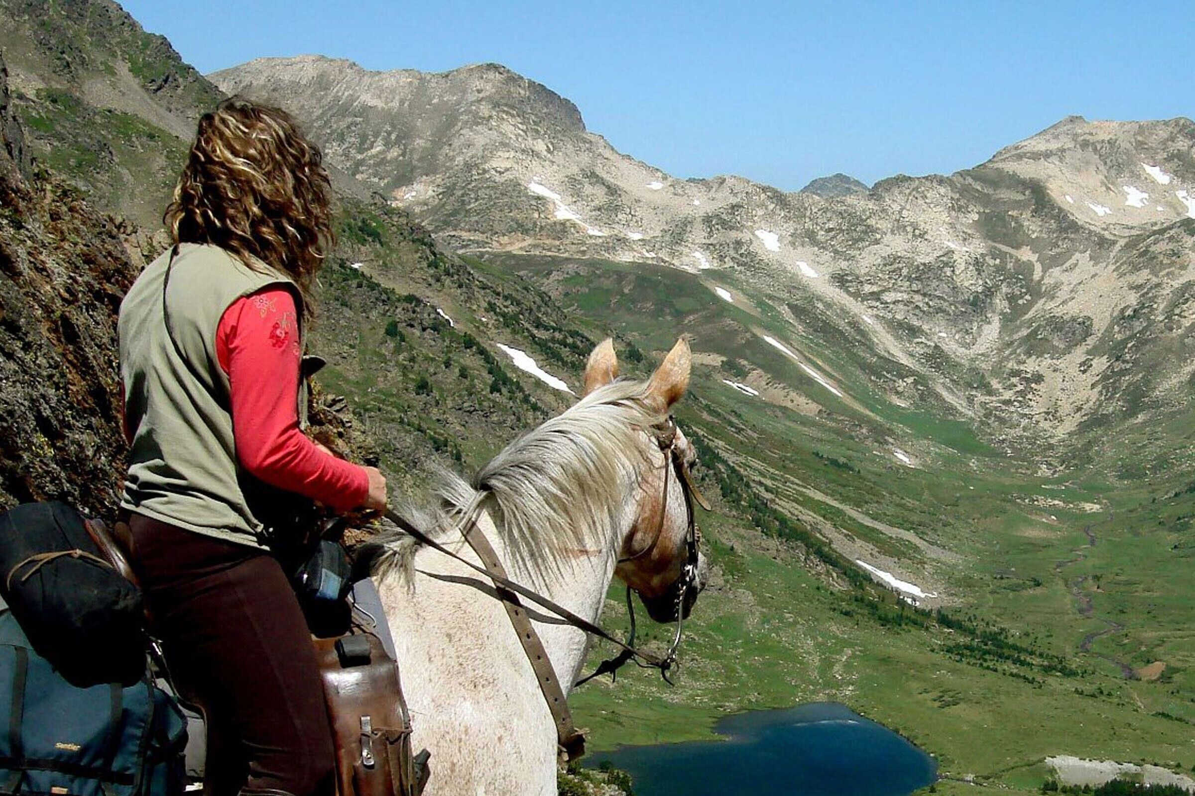 Una persona montando a caballo por un sendero de montaña, con una vista despejada del paisaje circundante.