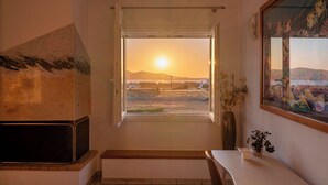 A room with a view of the sunset, a fireplace, a bench, and a painting on the wall. - Where the sea meets the sky your dream home in Paros with a view that never ends (Kampos)