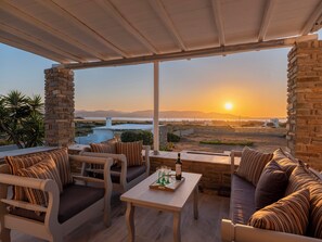 A terrace with outdoor seating, a table with glasses and a bottle, and a view of the sunset over a landscape. - Where the sea meets the sky your dream home in Paros with a view that never ends (Kampos)