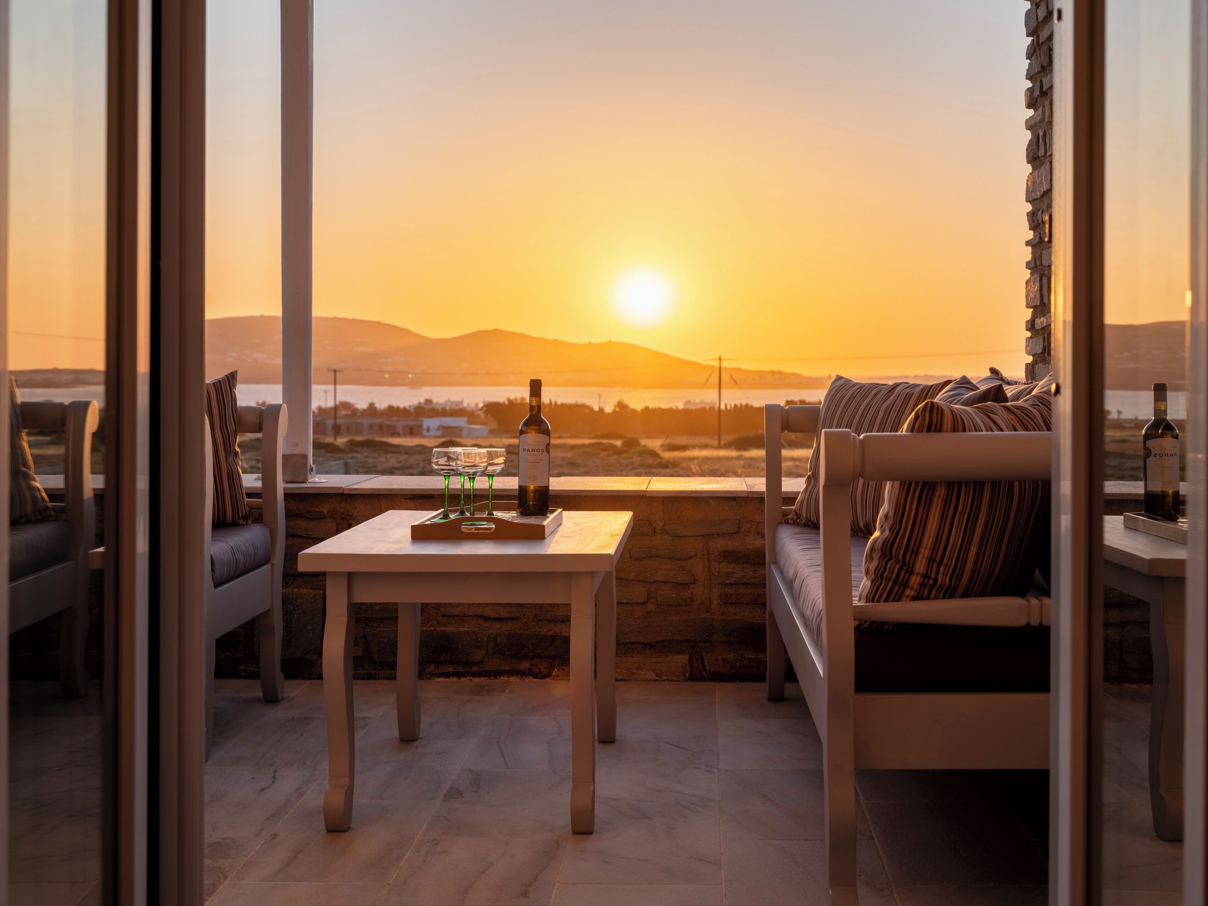 Un balcón con una mesa, un sofá y una botella de vino, con vistas a un hermoso atardecer.