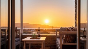 A balcony with a table, a sofa, and a bottle of wine, overlooking a scenic sunset view. - Where the sea meets the sky your dream home in Paros with a view that never ends (Kampos)