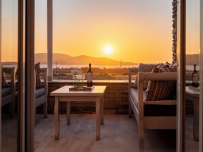 Ein Balkon mit Tisch, einer Couch und einer Weinflasche, mit Blick auf einen malerischen Sonnenuntergang.