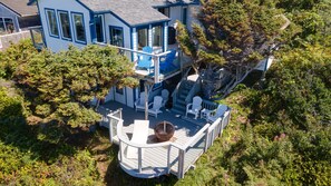 A two-story house with a deck, multiple windows, and a large tree in the background. - Pelican's Perch at Neskowin Ocean View (Cloverdale)