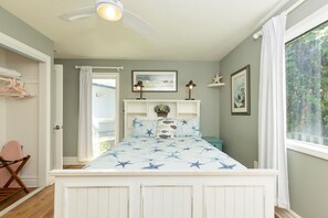 A bedroom with a bed, a ceiling fan, a window with curtains, a dresser, and a chair. - Pelican's Perch at Neskowin Ocean View (Cloverdale)