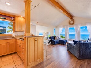 A spacious living area with a view of the sea, wooden flooring, and a kitchen with wooden cabinets. - Pelican's Perch at Neskowin Ocean View (Cloverdale)