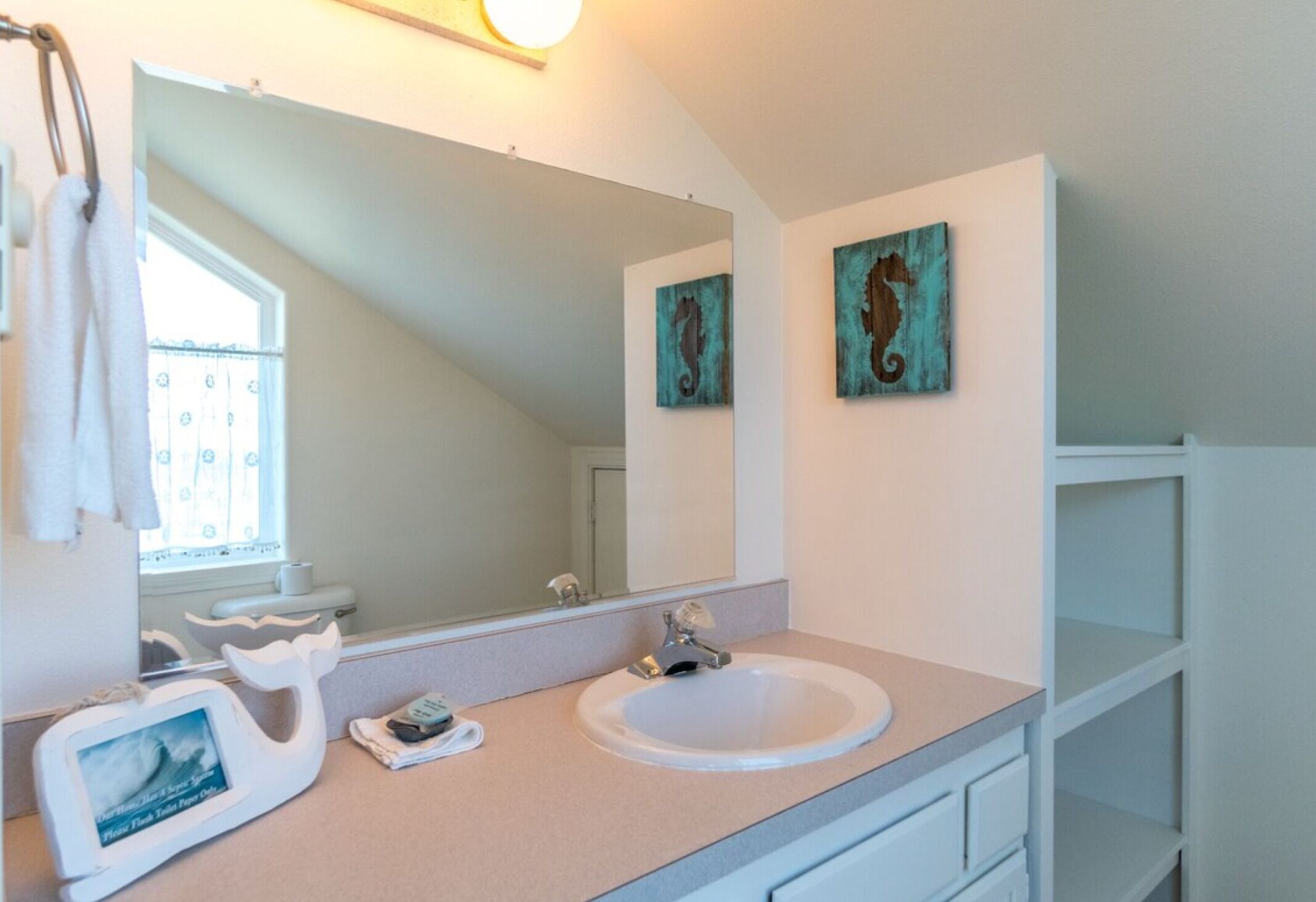 A bathroom with a white sink, a mirror, a towel rack, and two wall-mounted artworks.