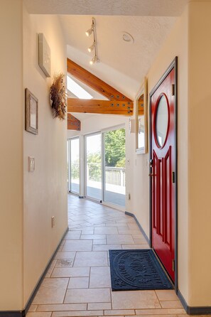 A hallway with a red door, a black doormat, and a wooden ceiling. - Pelican's Perch at Neskowin Ocean View (Cloverdale)