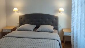 Et soveværelse med en stor seng, to sengeborde, en hængende lampe og et vindue med gardiner.