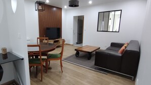 En moderne stue med sofa, sofabord, spisebord med stole, fjernsyn og køleskab.
