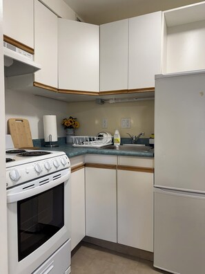 A kitchen with white cabinets, a stove, a sink, and a refrigerator.