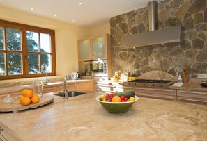 A modern kitchen with a stone backsplash, a large window, and a bowl of fruit on the counter. - All About Rif View Villa (Málaga)