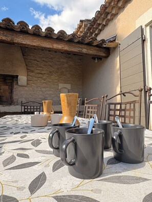 A courtyard with a tiled roof, stone walls, and a table with black mugs and a woven basket. - Charming, quiet house - heated pool-5 minutes from pretty village of Eygalières (Orgon)