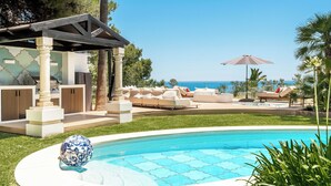 Een zwembadgedeelte met een pergola, lounge fauteuils en uitzicht op de oceaan.