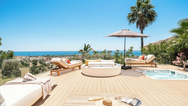 Een houten terras met lounge stoelen, een jacuzzi en uitzicht op zee.