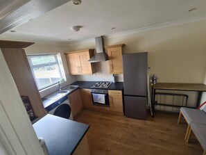 Eine kleine Küche mit Holzausstattung, einem Gasherd, einem Kühlschrank und einem Fenster mit Jalousien.