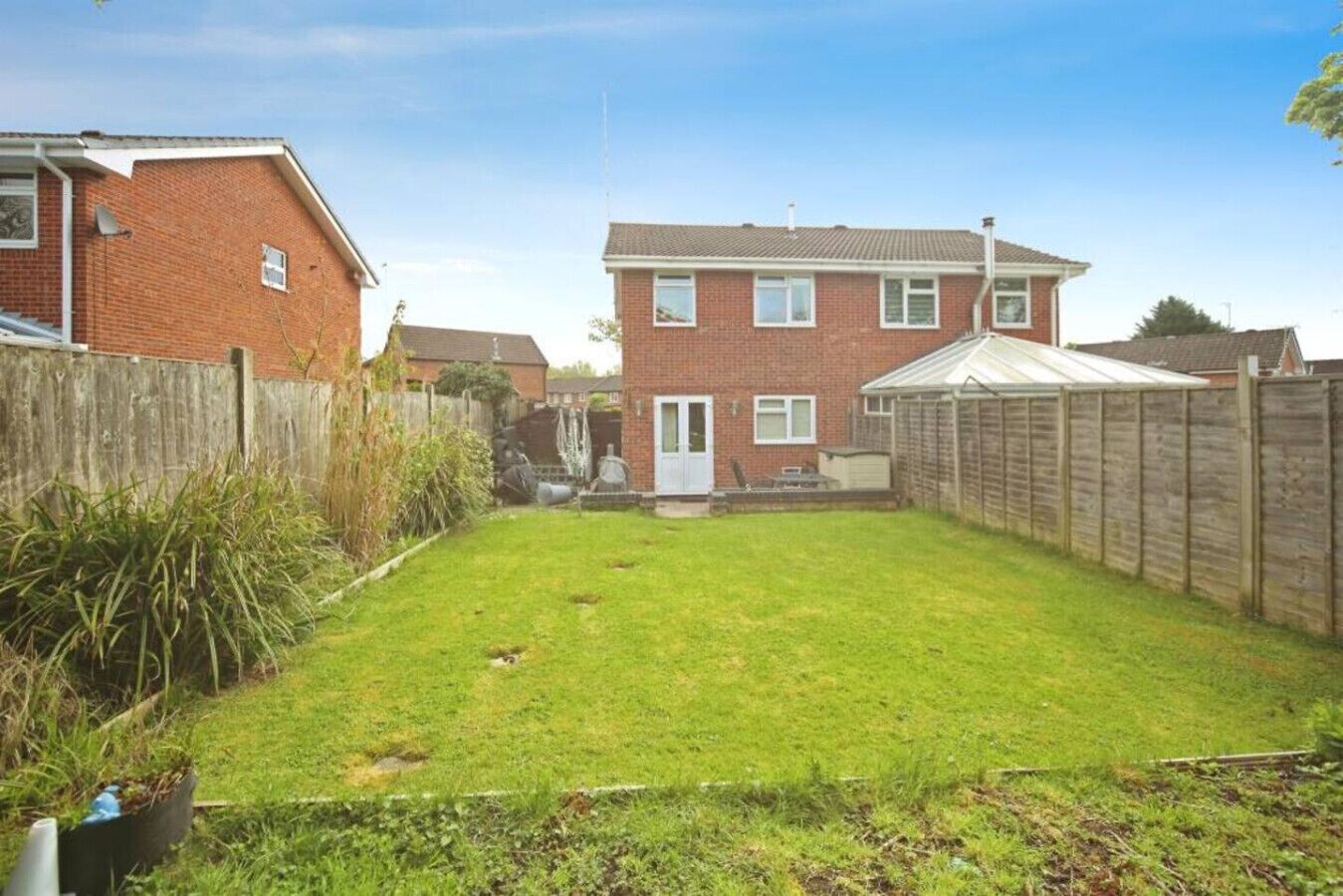 A residential backyard with a lawn, a wooden fence, and a brick house.