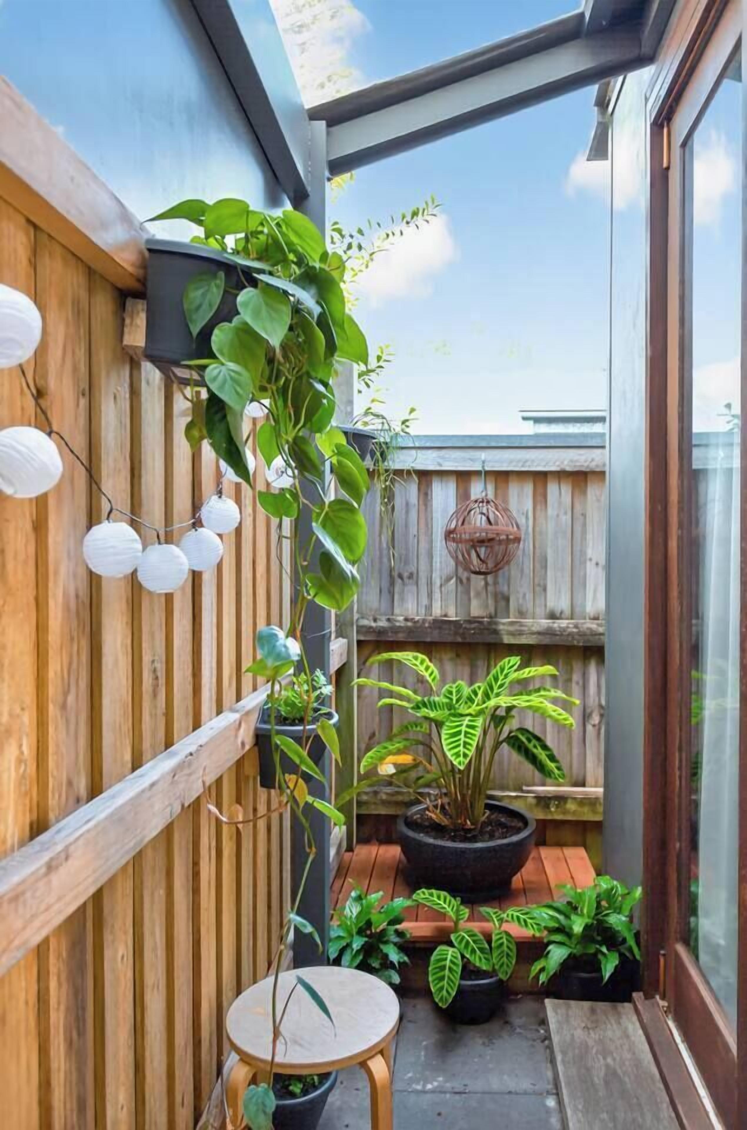 A small, enclosed outdoor space with a wooden fence, potted plants, a small table, and hanging lights.
