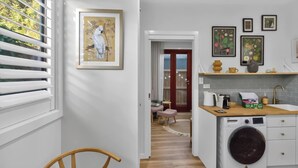 A compact kitchen with a washing machine, a small dining area, and a hallway leading to a door. - The Little Erko A Gateway to Sydneys Indie Heart (Newtown)