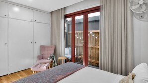 A bedroom with a bed, a chair, a wardrobe, and a sliding glass door leading to an outdoor area. - The Little Erko A Gateway to Sydneys Indie Heart (Newtown)