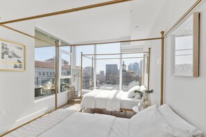 Een moderne slaapkamer met een groot raam, een hemelbed en uitzicht op de stad.