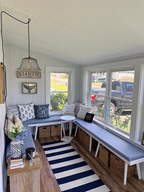 A cozy reading nook with a bench, books, and a view of the outside. - Beautiful 3 Bedroom Cottage steps from the Beach with brand new Trex deck (East Lyme)