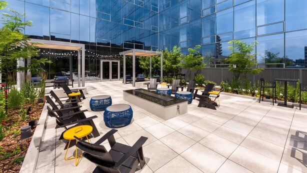 A modern outdoor patio with seating, a water feature, and a glass building facade. - Downtown Stamford Luxury | Indoor Pool & Gym (Stamford, CT)